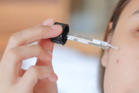 Asia woman sitting on bed and applying serum on face.