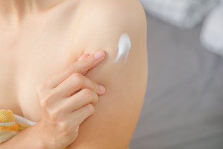 Asia woman sitting on bed and applying cream on her arm.
