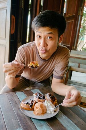 Man smiling eating waffle with ice-cream at vintage cafe.の写真素材