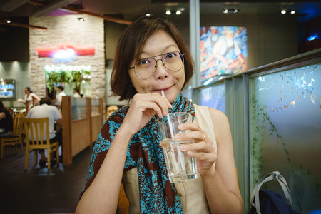 Woman Looking Toward Camera Whilst Drinking Water In Restaurant.