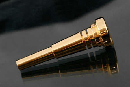 Gold plated trumpet mouthpiece on a shiny surfaceの写真素材