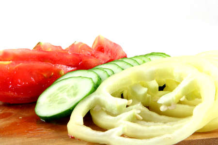Tomatos cucumbers and a yellow pepper on a wooden plate isolated on whiteの写真素材