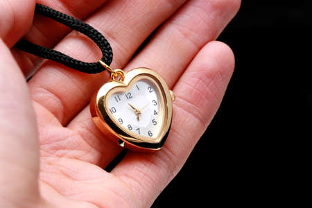 Hand holding a small golden watch in a heart shapeの写真素材