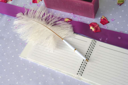 Pink notebook and a feather pen on a wedding guest tableの写真素材