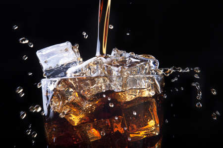 Fresh cola drink background with ice and splash on a blackの写真素材
