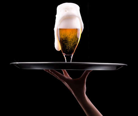waiter hand and tray with Beer into glass on a blackの写真素材