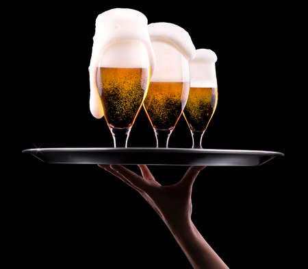 waiter hand and tray with Beer into glass on a blackの写真素材