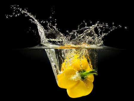 Yellow bell pepper falling in water with splash on black background.の写真素材