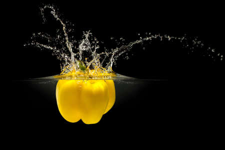 Yellow bell pepper falling in water with splash on black background.の写真素材