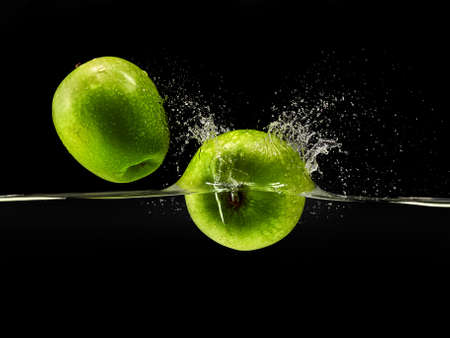 Group of green apples falling in water with splash on black background.の写真素材