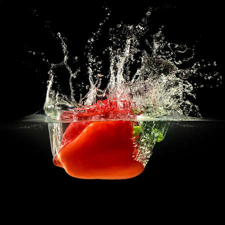 Red bell pepper falling in water with splash on black background.の写真素材
