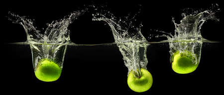 Green apple falling in water on black background
