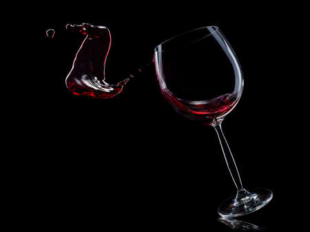 Glass for red wine with splashes isolated on black background.