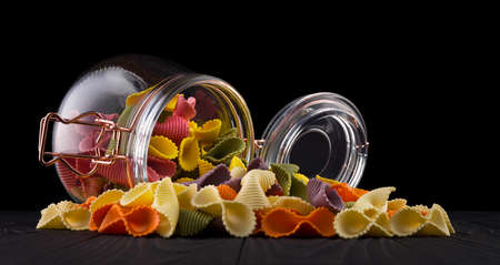 Jar of colorful farfalle pasta on wooden table isolated on black background