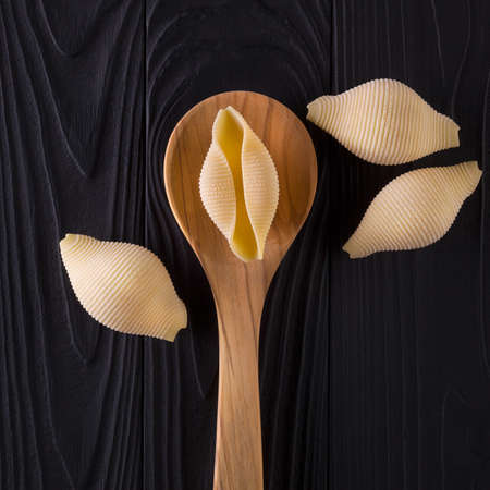 Top view of conchiglie pasta shells on black wooden table with spoonの写真素材