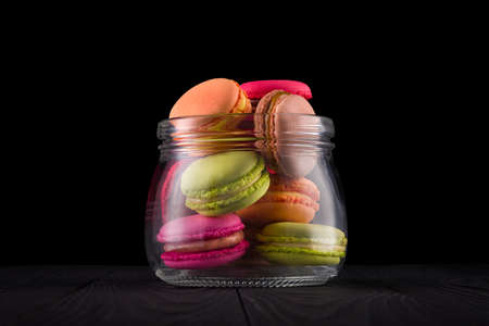 Jar of french colorful macaroon or macaron on wooden table isolated on black