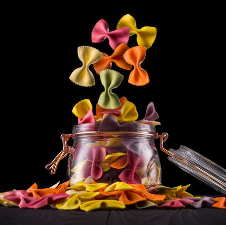 Jar of colorful farfalle pasta on wooden table isolated on black backgroundの写真素材