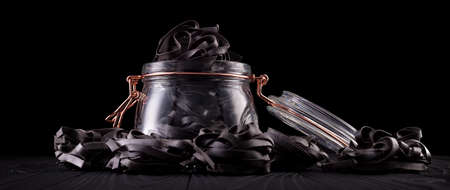 Jar of tagliatelle pasta nests on wooden table isolated on black