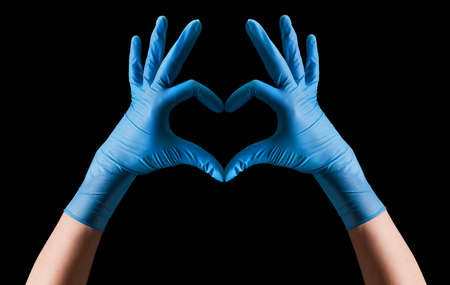 Doctors hand in sterile medical gloves showing heart shape isolated on black