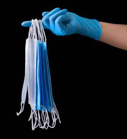 Doctors hand in medical gloves holding a pile of masks isolated on black
