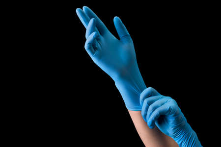 Doctor wearing a medical glove on hands isolated on black