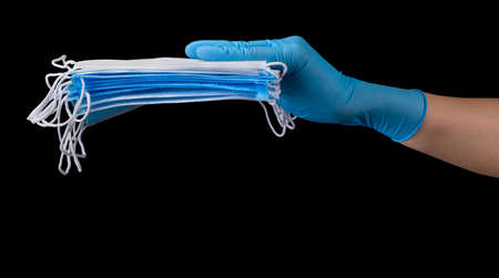Doctor's hand in medical gloves holding a pile of masks isolated on black background with clipping...