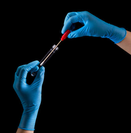 Doctor's hands in medical gloves holding test tube with coronavirus COVID-19 isolated on black...