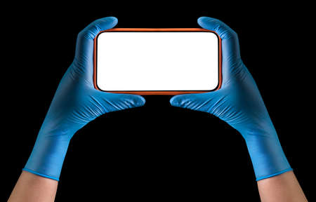 Doctor's hand in sterile medical gloves holding phone playing games isolated on black background . Concept of protection against pandemic and virusesの写真素材