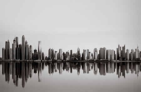 Monochrome city skyline with tall skyscrapers reflecting on calm water under a cloudy sky, concept of urban development, Dubai Marina bay UAEの写真素材