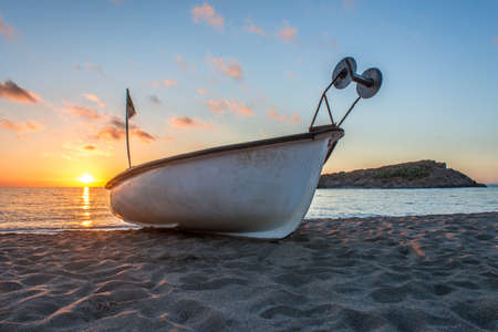 A fishing boat on the sands of the Mediterranean sea . A fishing boat on the beach at sunset. Wooden boat opposite a small islandの写真素材