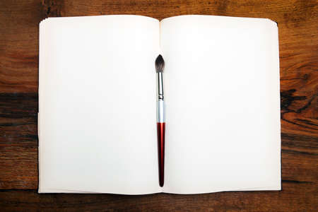 Vintage book, open, on old wooden table with paint brush.