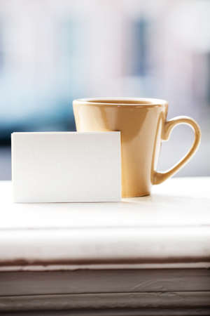 Business card on windowsill against a cup, city view behind.の写真素材