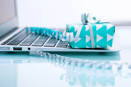 Gift box with silver bow on light background next to the computer. On line shoppingの写真素材