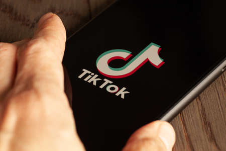 TikTok application icon on Apple iPhone 11 screen close-up. Hand holding smartphone Tik Tok icon on...