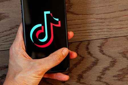 TikTok application icon on Apple iPhone 11 screen close-up. Hand holding smartphone Tik Tok icon on...