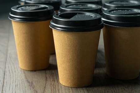 Disposable cups of coffee on a wooden table. Brown paper cup with black lidの写真素材