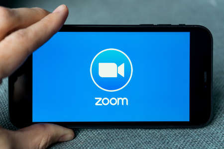 Phone with a hand showing Zoom Cloud Meetings app. Work and have meetings from home with a smart phone.のeditorial素材