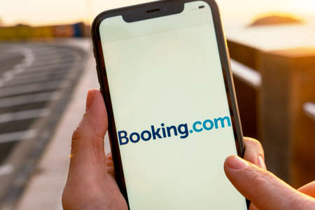 Hands holding iPhone 11 with an app of booking.com service. Holidays and vacation concept. A woman...