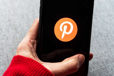 Young woman holding a smartphone with Pinterest app on screen. IPhone 11 with a social media app logo for interesting and exceptional content.のeditorial素材