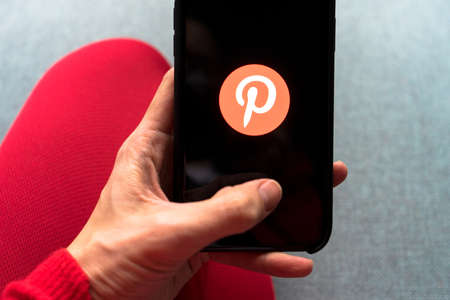 Young woman holding a smartphone with Pinterest app on screen. IPhone 11 with a social media app...