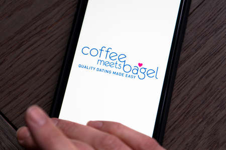 Young woman holding a smartphone with Coffee meets bagel dating app on screen. IPhone 11 with a...