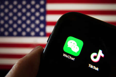 Cellphone with WeChat and TikTok icons in front of the flag of America. USA president Donald Trump...