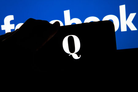 QAnon vs FACEBOOK. QAnon organization logo seen on the smartphone which is placed on Facebook logos....