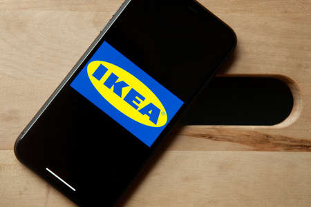 Logo of Ikea on iPhone 11 screen on a wooden bench. Largest interior design company and store starts a second hand, used furniture market.のeditorial素材