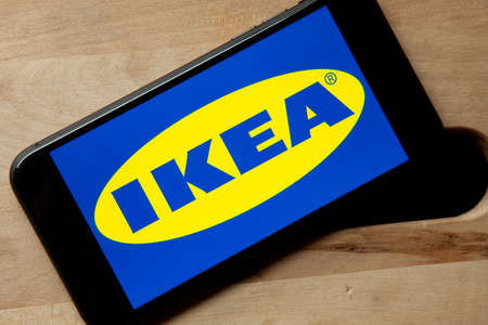 Logo of Ikea on iPhone 11 screen on a wooden bench. Largest interior design company and store starts a second hand, used furniture market.のeditorial素材