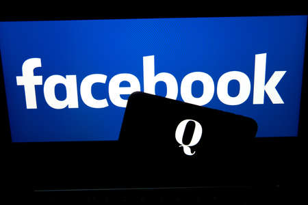 QAnon vs FACEBOOK. QAnon organization logo seen on the smartphone which is placed on Facebook logos....