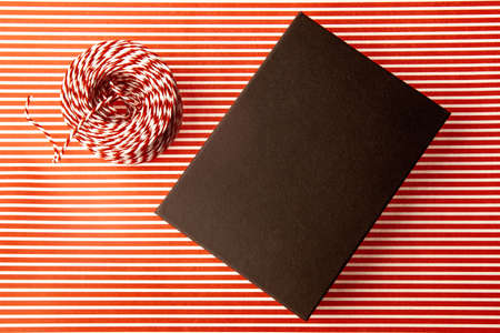Close-up of present. Black box, resent packaging paper with red and white stripes and striped cord....