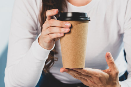 Young woman in white shirt and denim jeans holds disposable coffee cup.の写真素材