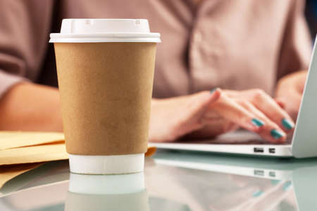 Close-up of a paper cup of coffee and laptop on the tableの写真素材