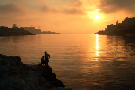 Silhouette of fishermen at sunrise, Malta, Europe.の写真素材